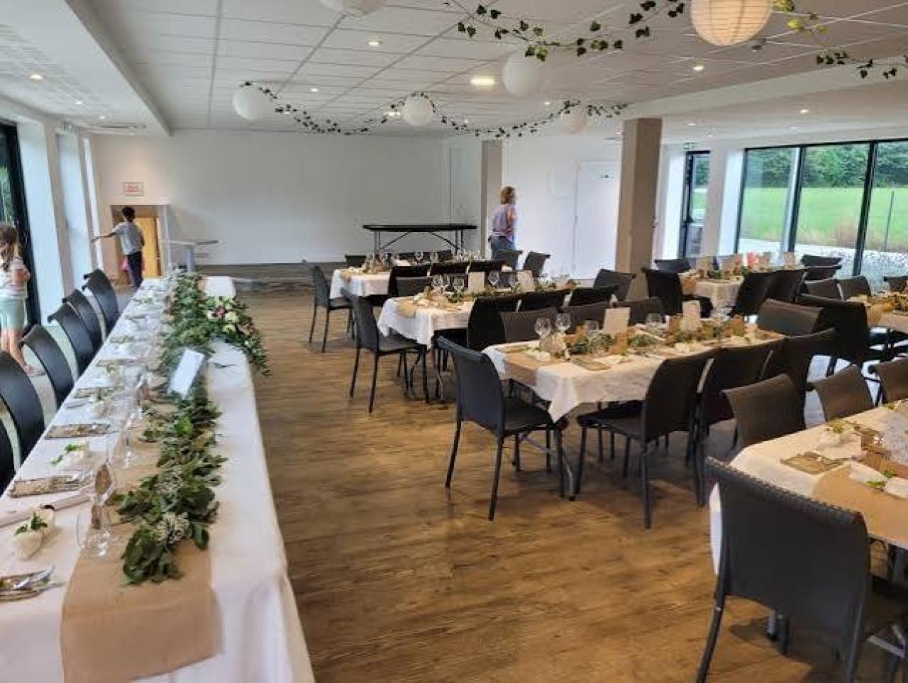 Salle de réception du Domaine de l'Aéropiste dressée pour un repas, tables nappées et décor végétal
